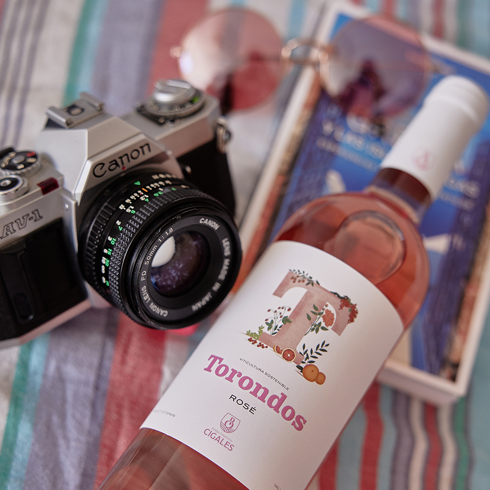 Botella Torondos Rosé en una mesa con una cámara de fotos, unas gafas de sol y un libro.