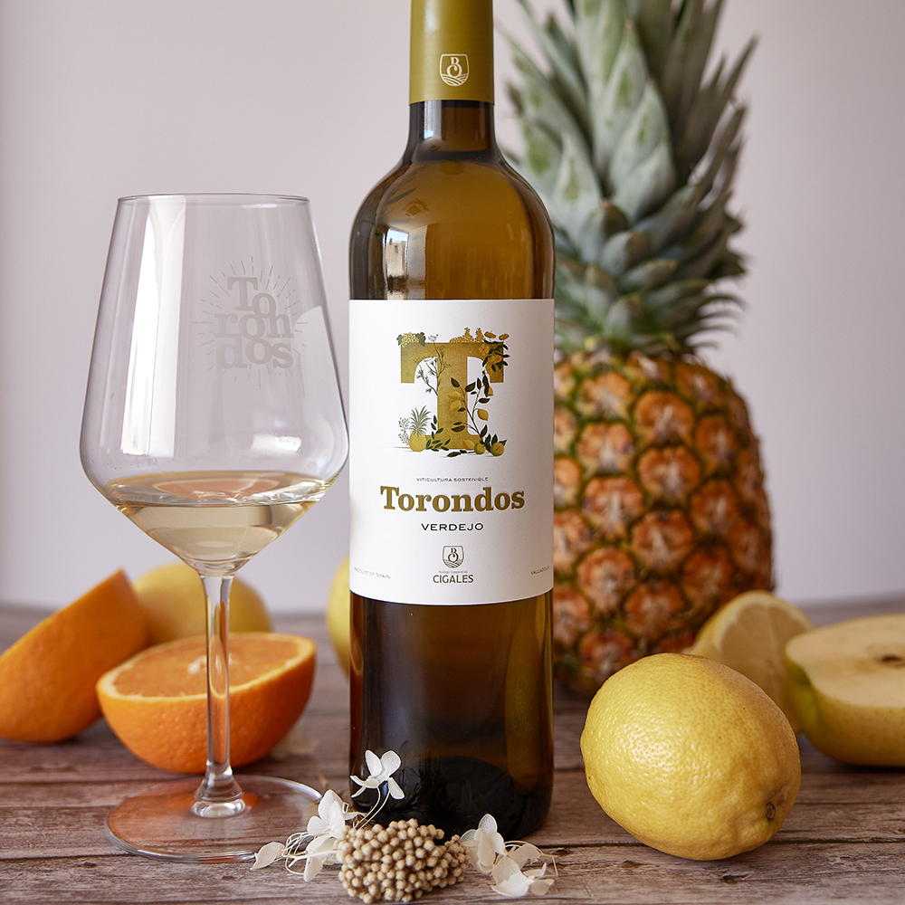 Botella Torondos Verdejo en una mesa con una copa de vino y frutas.